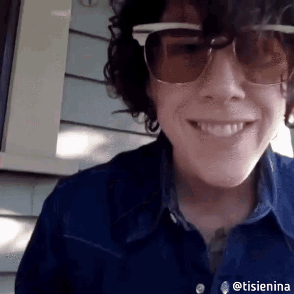 a woman wearing sunglasses and a blue shirt has the hashtag @tisienia on the bottom of her shirt