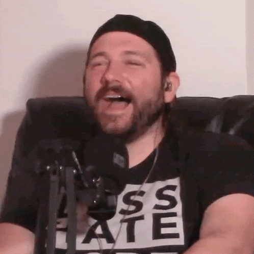 a man with a beard wearing a t-shirt that says " ass ate " is singing into a microphone