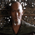 a bald man with a beard is sitting in front of a carved wall .