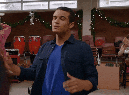 a man in a blue shirt is dancing in a room with drums in the background