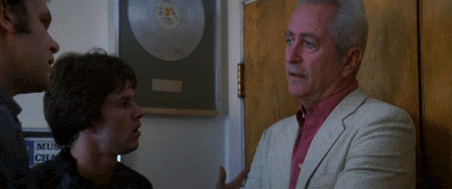 a man in a suit is talking to two other men in front of a sign that says music club