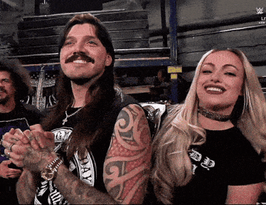 a man with a mustache is smiling next to a woman who is wearing a black shirt that says " day " on it
