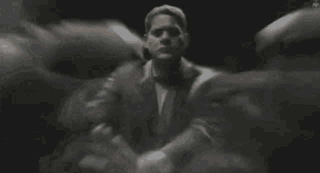 a man in a suit and tie is standing in a dark room with a blurred background .