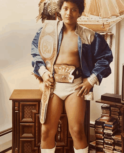 a young man wearing a wrestling belt stands in front of a stack of cd 's