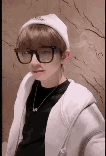 a young man wearing glasses and a beanie is taking a picture of himself .
