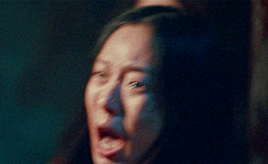 a woman is crying with her eyes closed in a dark room while another woman looks on .