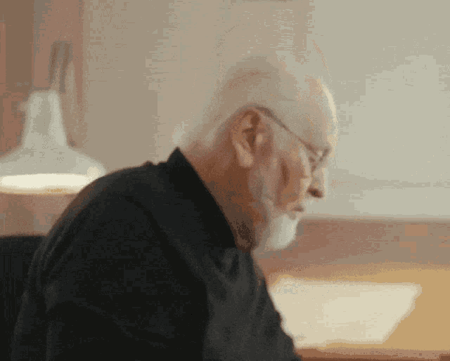a man with white hair and a beard is sitting at a desk