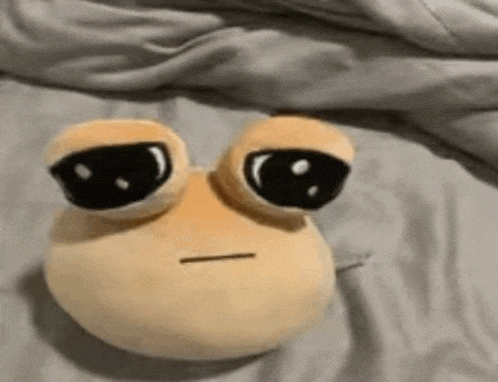 a stuffed frog with big eyes is laying on a bed .