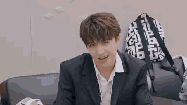 a young man in a suit is sitting on a couch and smiling .