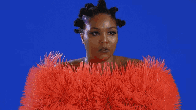 a woman is wearing a red feathered coat against a blue backdrop