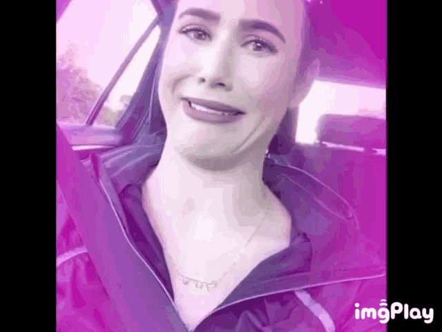 a woman is making a funny face while sitting in a car with a purple background .
