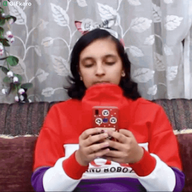 a girl is sitting on a couch holding a cell phone in front of her face .