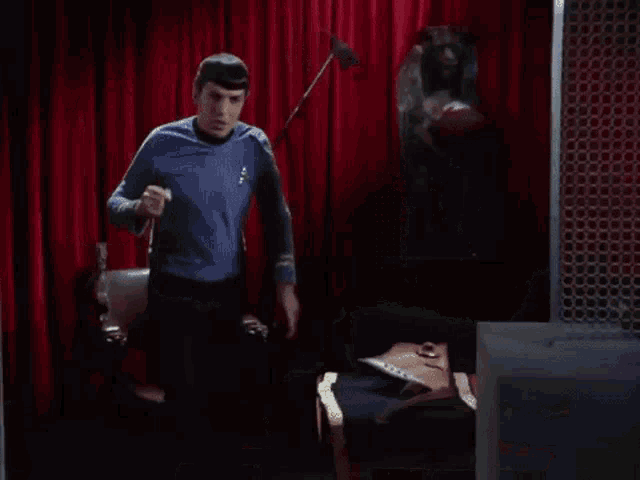 a man in a blue shirt is standing in a room with a red curtain behind him .