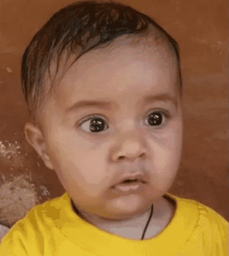 a baby wearing a yellow shirt is making a funny face .