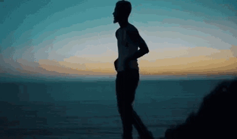 a man is standing on top of a cliff overlooking the ocean at sunset .