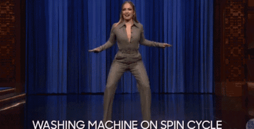 a woman in a suit is dancing on a stage with the words washing machine on spin cycle below her .