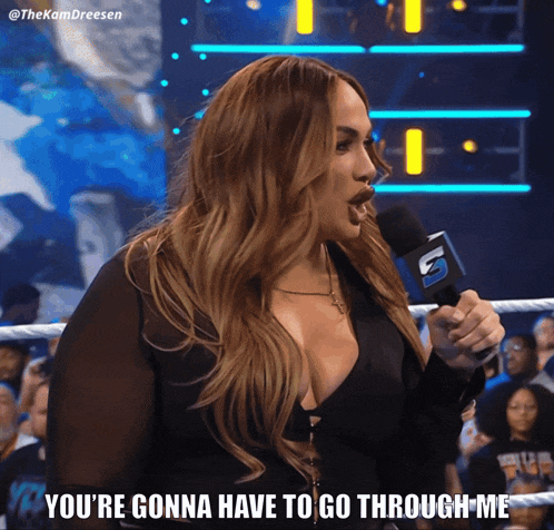 a woman in a wrestling ring is holding a microphone and says you 're gonna have to go through me