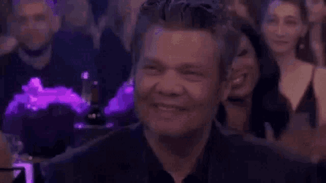 a man is smiling in front of a crowd of people at a party .