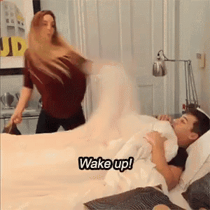 a man and a woman are having a pillow fight on a bed and the woman is saying " wake up "