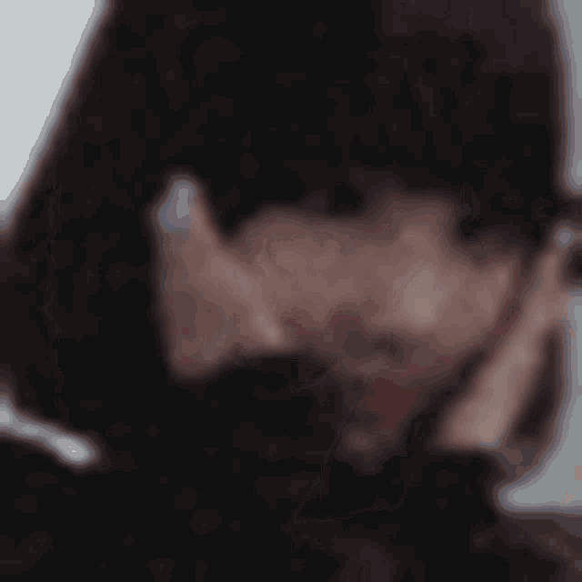 a blurry picture of a person 's face with their hands on their face .