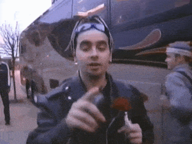 a man in a leather jacket is holding a red flower in front of a bus