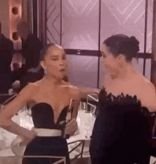 two women are standing next to each other in a room and talking .