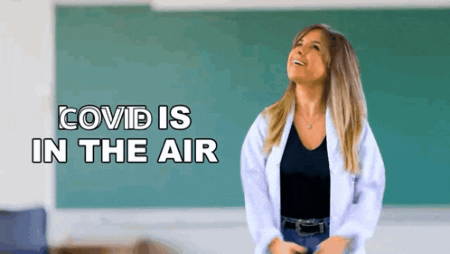 a woman in a lab coat is standing in front of a chalkboard with the words covid is in the air .
