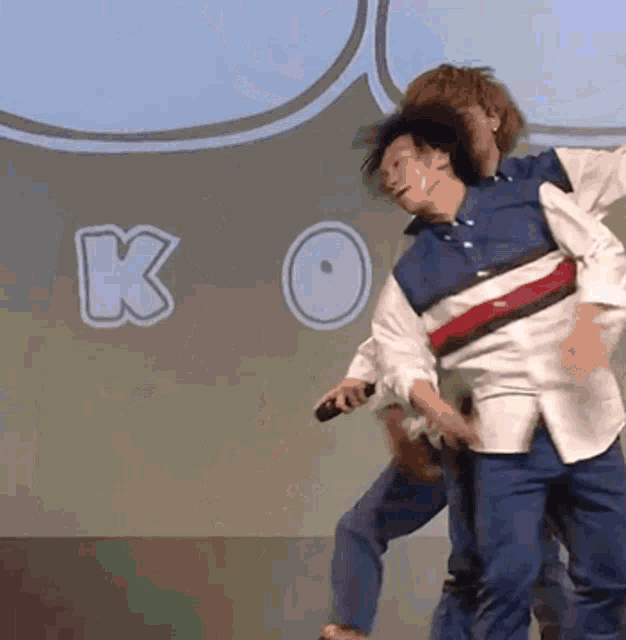 two men are dancing in front of a sign that says ko