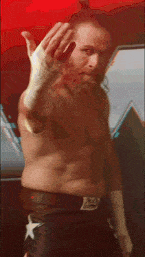 a man without a shirt is saluting in front of a red wall