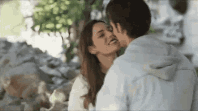a man is kissing a woman on the forehead in front of a tree
