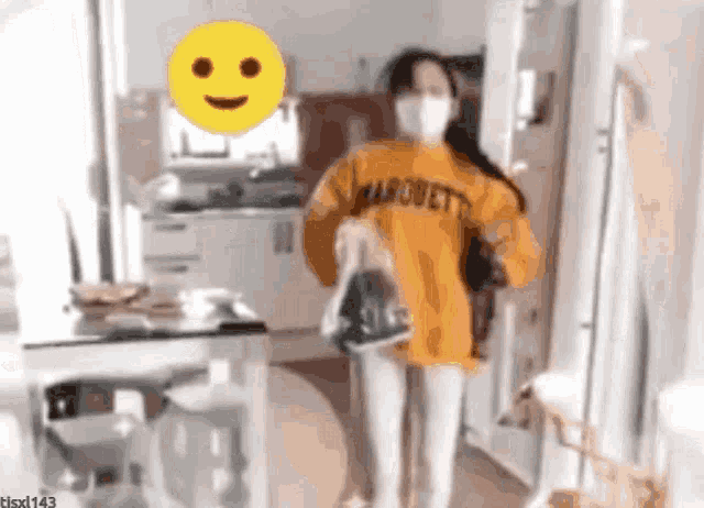 a woman wearing a mask and a marquette sweatshirt is holding a bag in a kitchen .