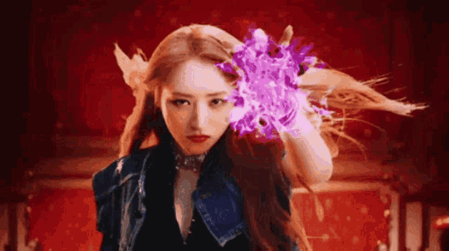 a woman is holding a purple flower in her hand and looking at the camera .