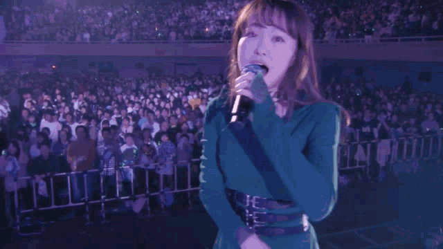a woman in a green dress sings into a microphone while a crowd watches