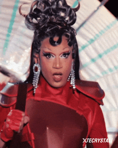 a drag queen is wearing a red outfit with xtecrystal written on the bottom right