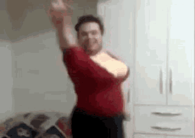 a man in a red shirt is dancing in a bedroom with his arm in the air .
