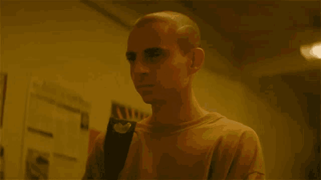 a man with a shaved head is standing in a hallway with posters on the wall behind him .