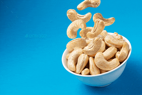 cashews falling into a white bowl with a blue background