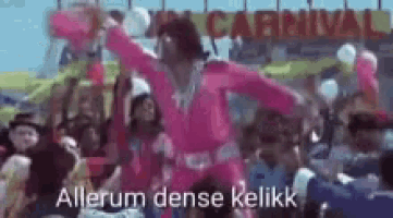 a man in a pink outfit is dancing in front of a crowd at a carnival .