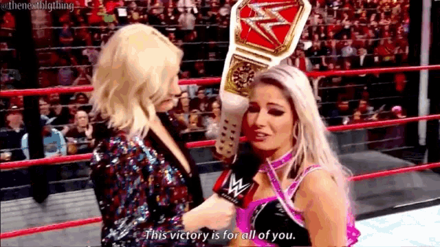 two women are standing in a wrestling ring and one of them is holding a championship belt .