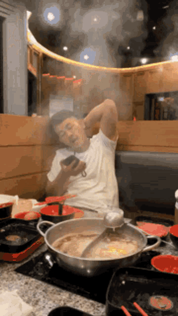 a man is sitting at a table with a pot of food and looking at his cell phone