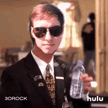 a man in a suit and tie is holding a bottle of water ..