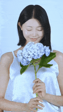 a woman in a white top holds a blue flower