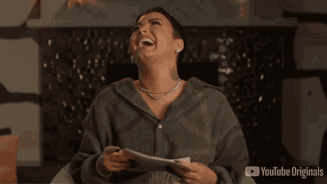 a woman laughs while holding a piece of paper with youtube originals on the bottom