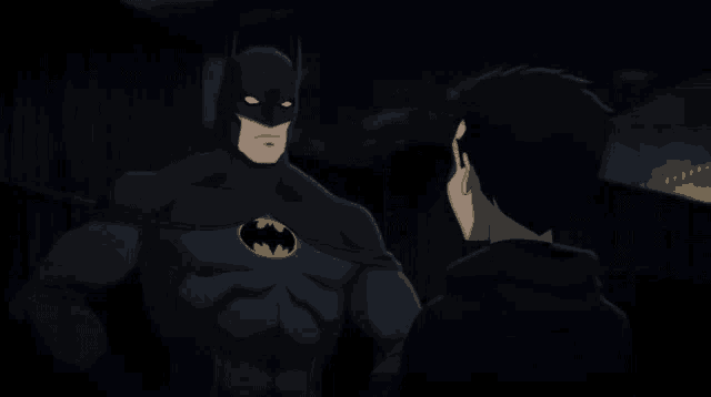 a man in a black batman costume talks to another man in a black hoodie
