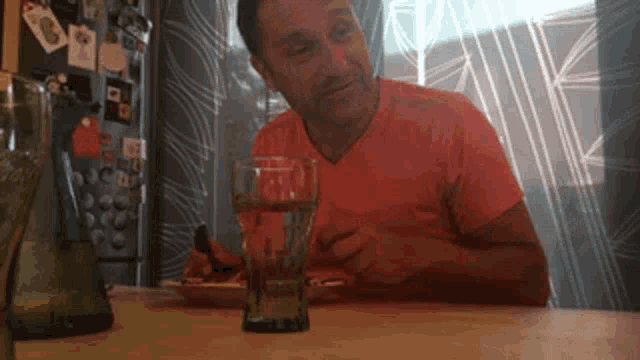 a man in a red shirt is sitting at a table with a glass of water in front of him .