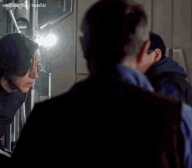 a man in a blue shirt is looking at another man in a dark room with the word tumblr on the bottom right