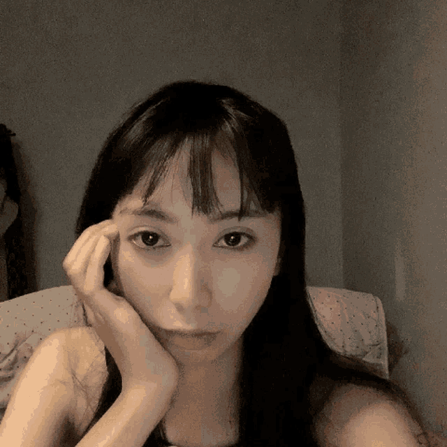 a woman with long black hair and bangs holds her hand to her face