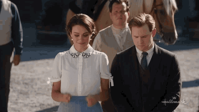 a man in a suit and tie stands next to a woman in a white shirt that says hallmark on the bottom