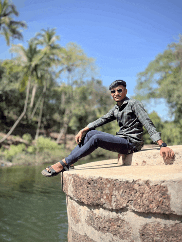 a man sits on a stone wall near a river