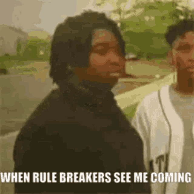 a man is standing next to another man with the words `` when rule breakers see me coming '' written on his face .